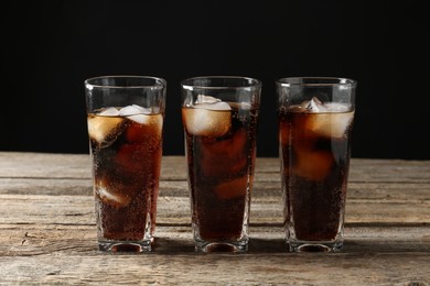 Photo of Refreshing cola with ice cubes in glasses on wooden table against black background