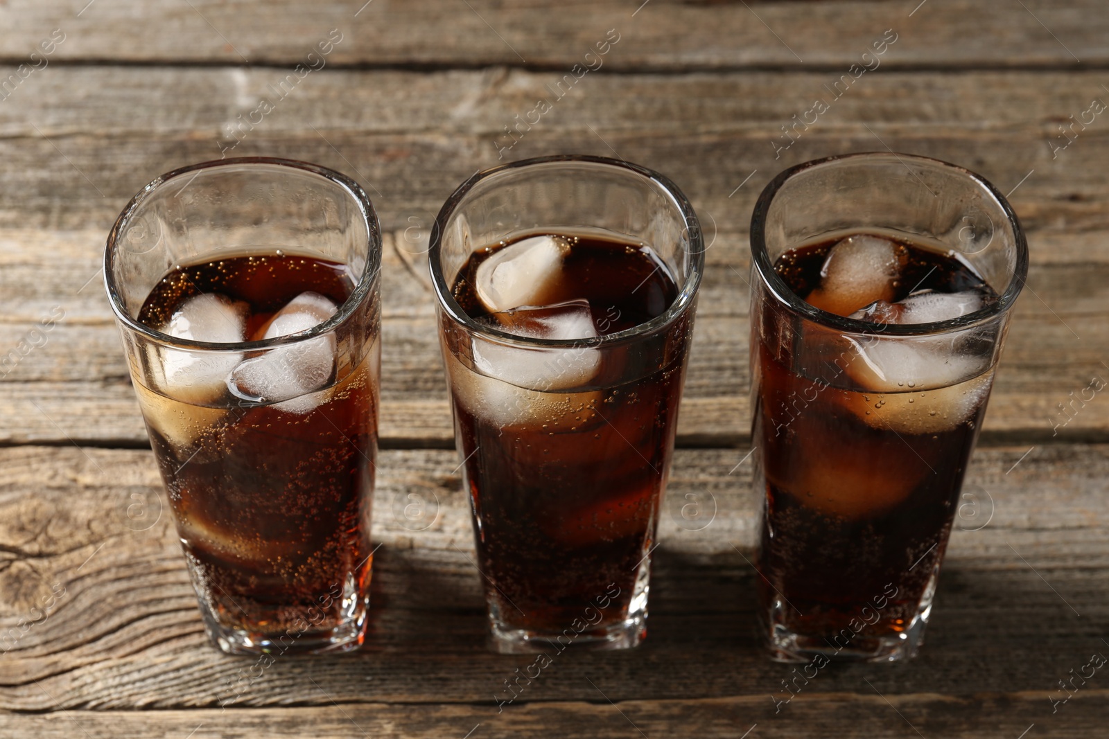 Photo of Refreshing cola with ice cubes in glasses on wooden table, closeup