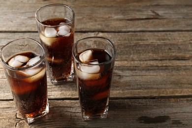 Photo of Refreshing cola with ice cubes in glasses on wooden table, closeup. Space for text