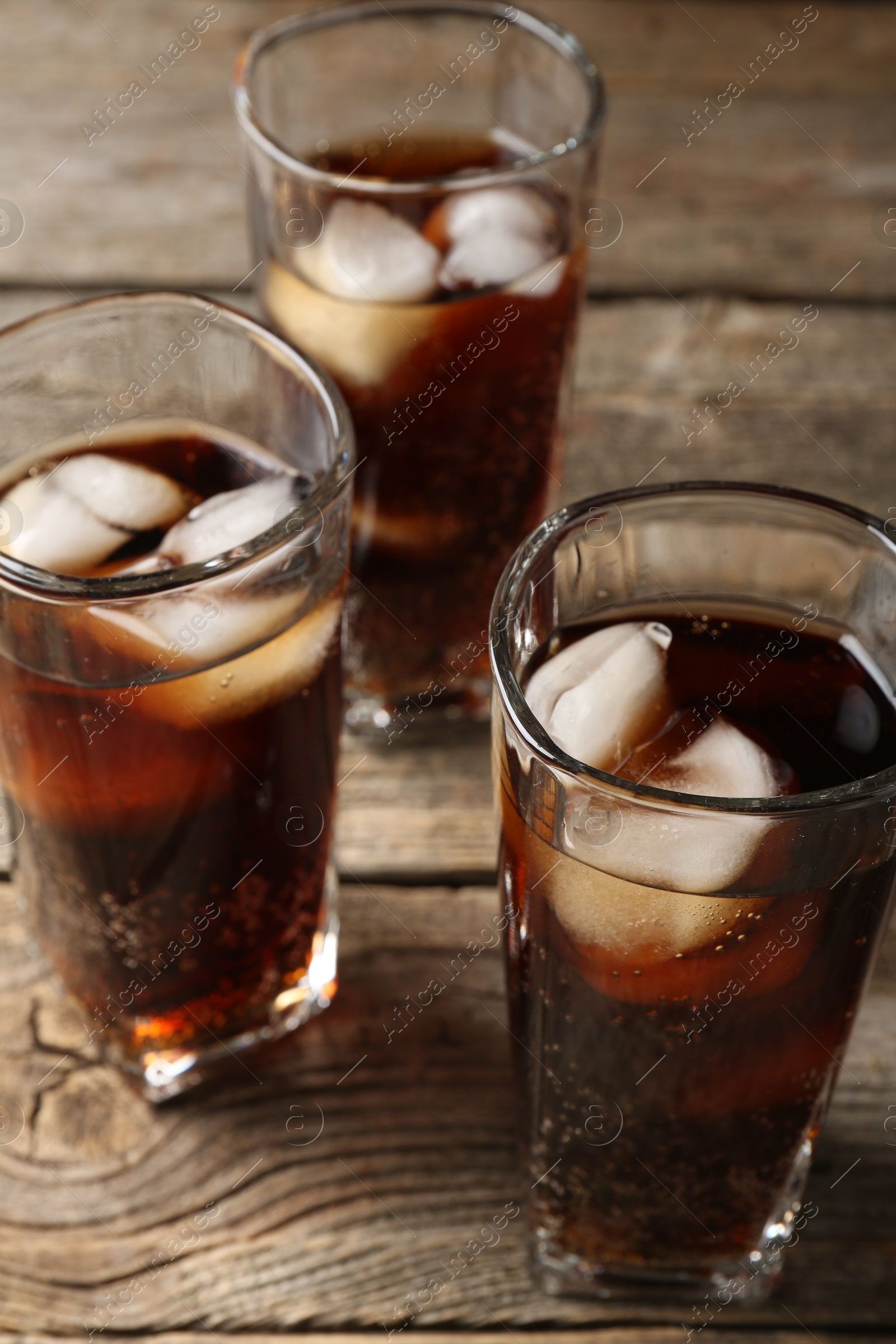 Photo of Refreshing cola with ice cubes in glasses on wooden table, closeup