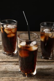 Photo of Refreshing cola with ice cubes and drinking straws in glasses on wooden table against black background, closeup