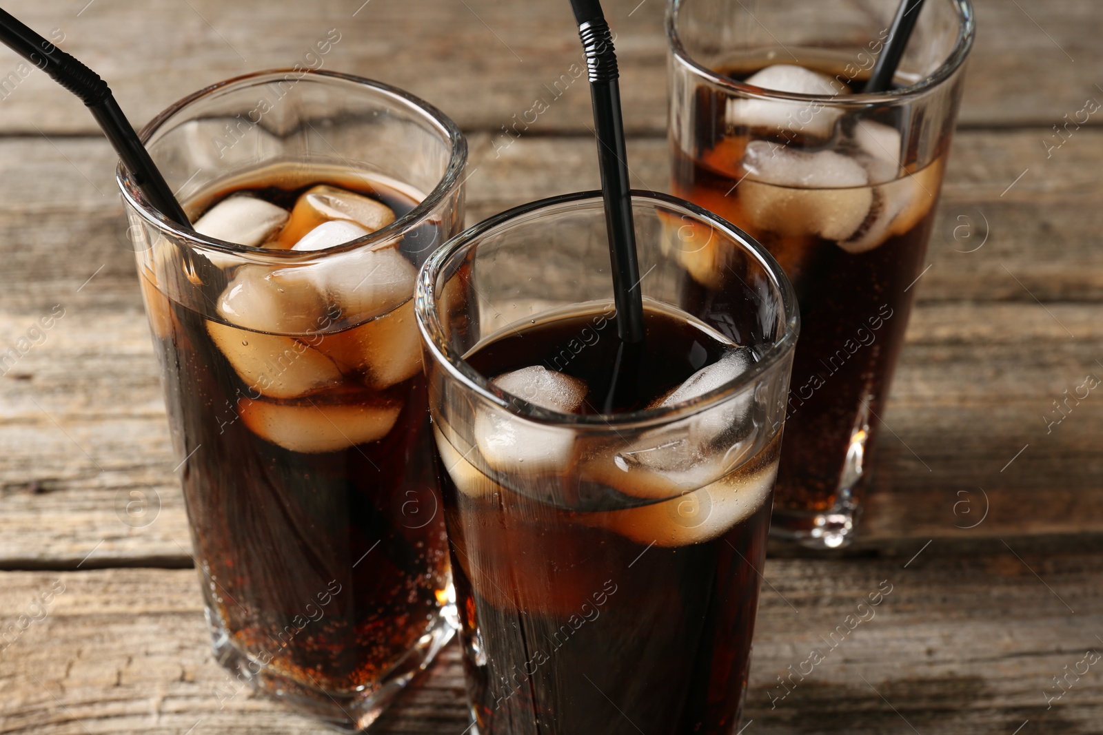 Photo of Refreshing cola with ice cubes and drinking straws in glasses on wooden table, closeup