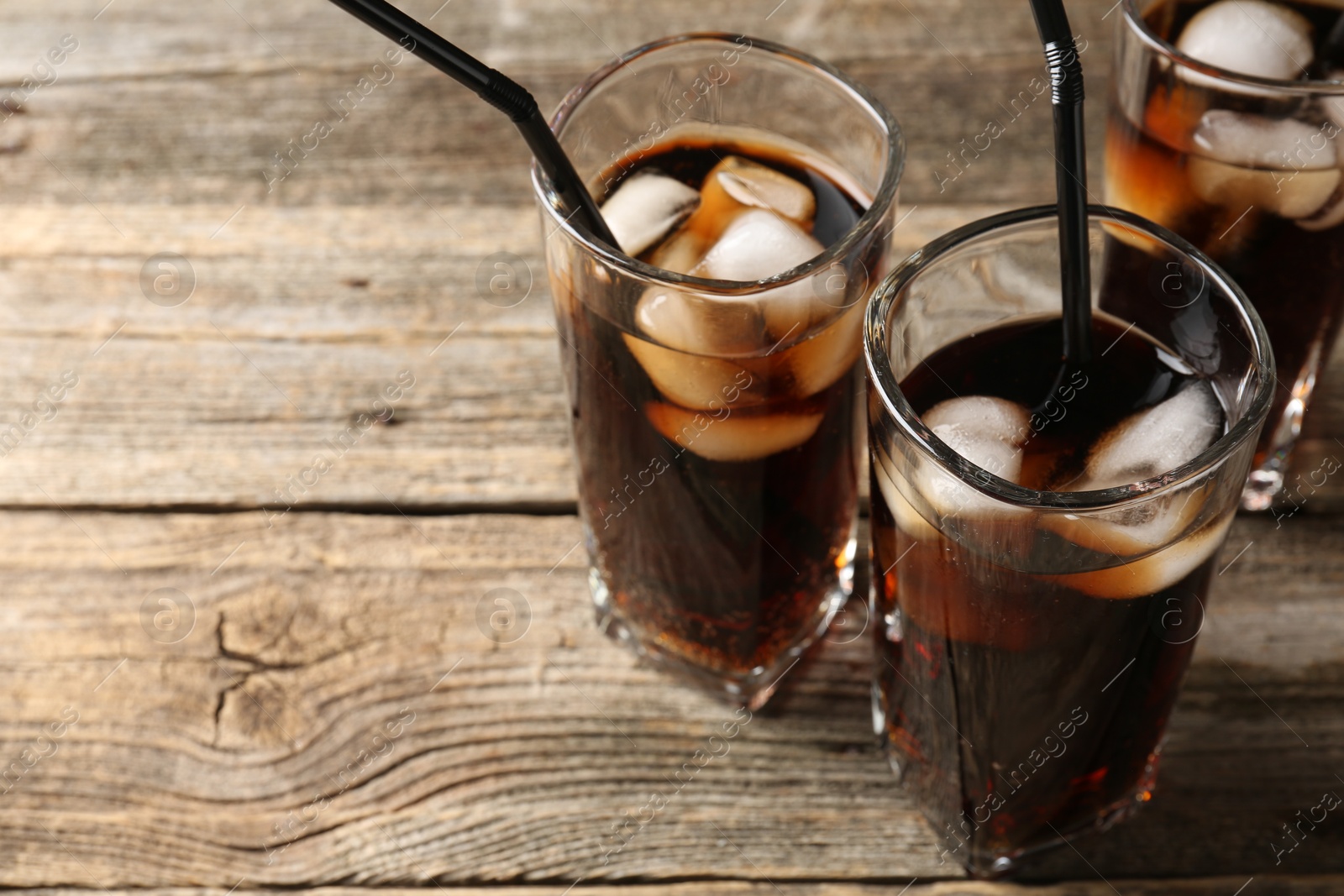 Photo of Refreshing cola with ice cubes and drinking straws in glasses on wooden table, closeup. Space for text