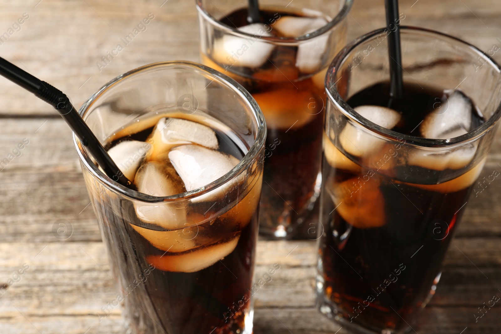 Photo of Refreshing cola with ice cubes and drinking straws in glasses on wooden table, closeup