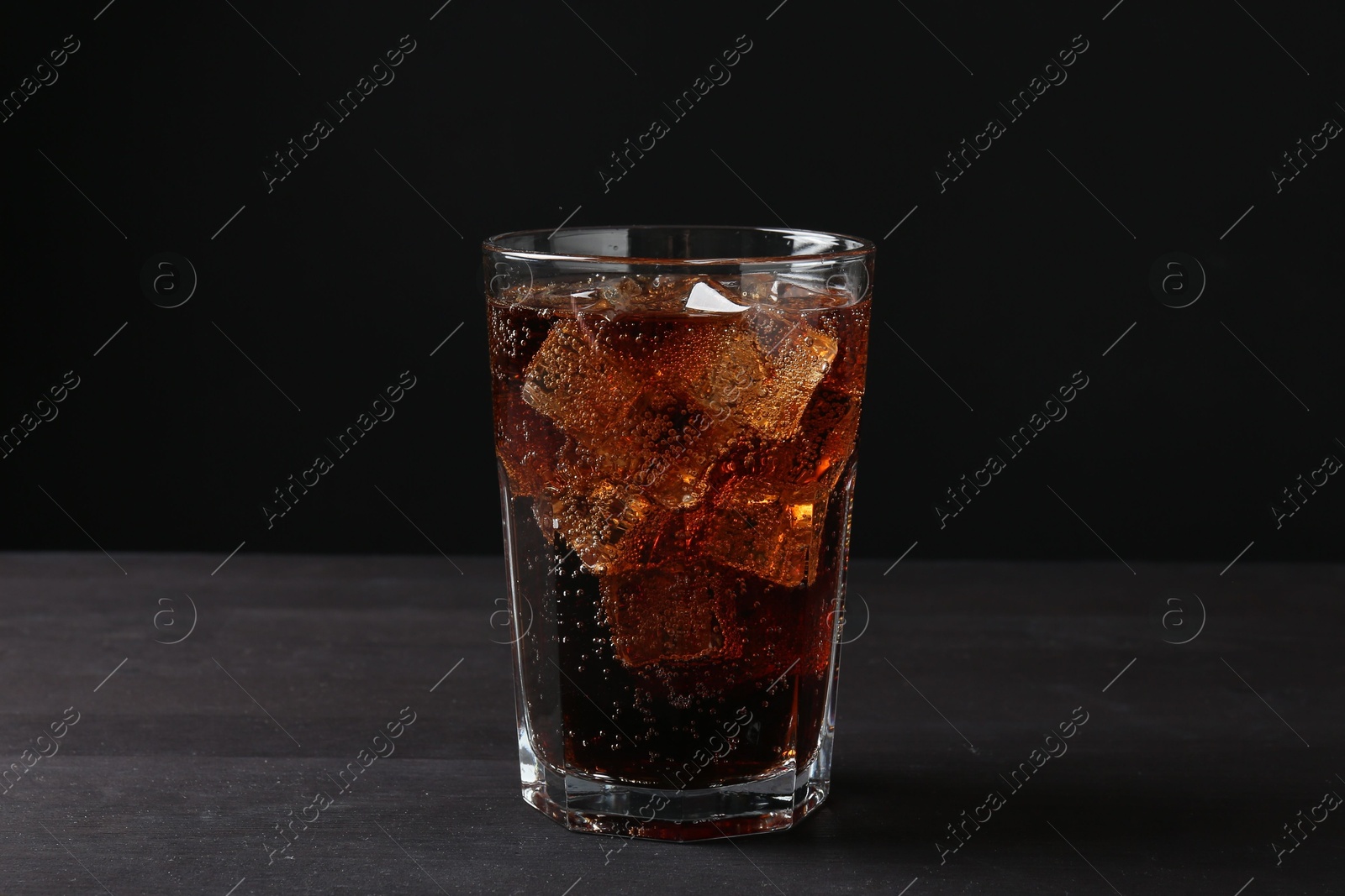 Photo of Refreshing cola with ice cubes in glass on black wooden table, closeup