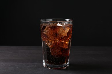 Photo of Refreshing cola with ice cubes in glass on black wooden table, closeup