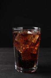 Photo of Refreshing cola with ice cubes in glass on black wooden table, closeup