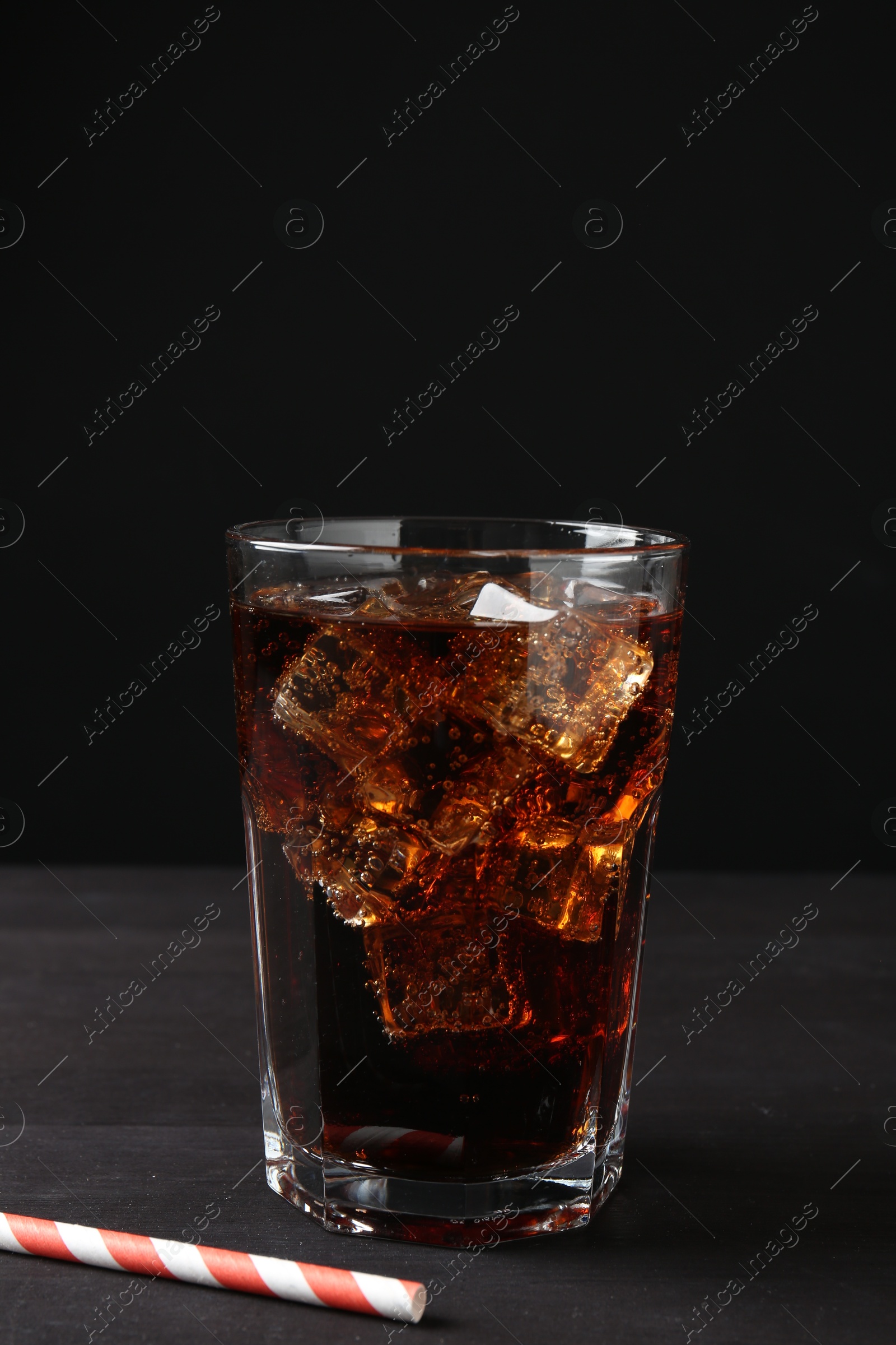 Photo of Refreshing cola with ice cubes in glass and drinking straw on black wooden table, closeup