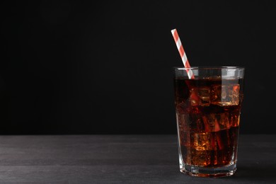 Photo of Refreshing cola with ice cubes and drinking straw in glass on black wooden table, closeup. Space for text