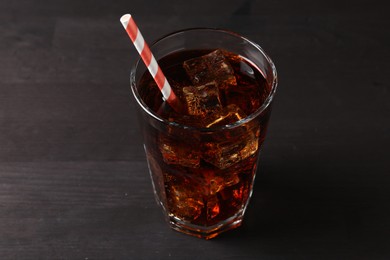 Photo of Refreshing cola with ice cubes and drinking straw in glass on black wooden table, closeup