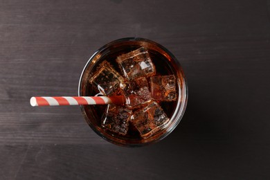 Photo of Refreshing cola with ice cubes and drinking straw in glass on black wooden table, top view