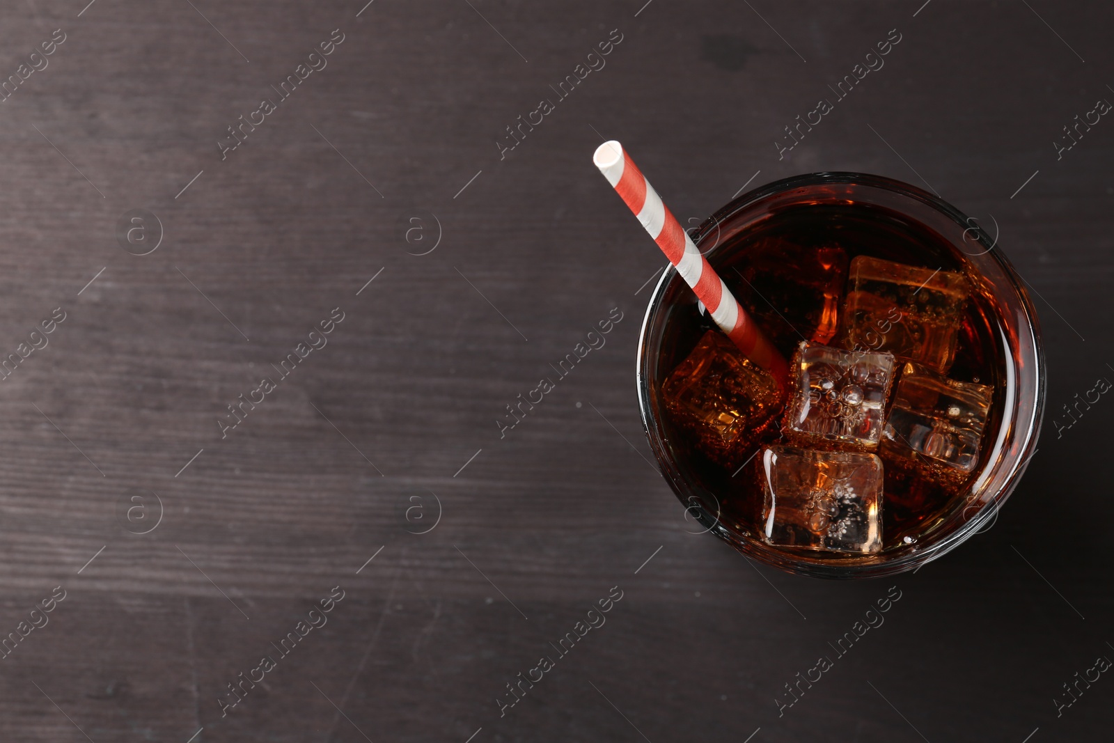 Photo of Refreshing cola with ice cubes and drinking straw in glass on black wooden table, top view. Space for text