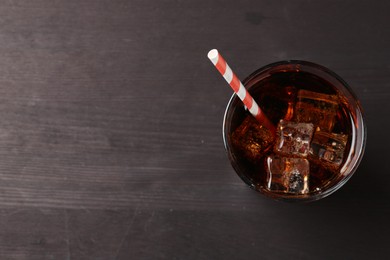 Photo of Refreshing cola with ice cubes and drinking straw in glass on black wooden table, top view. Space for text