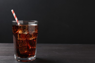 Photo of Refreshing cola with ice cubes and drinking straw in glass on black wooden table, closeup. Space for text