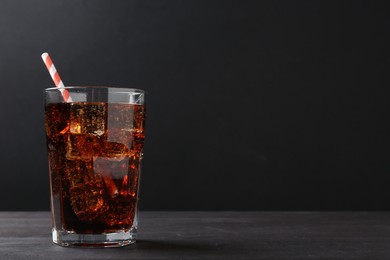 Photo of Refreshing cola with ice cubes and drinking straw in glass on black wooden table, closeup. Space for text