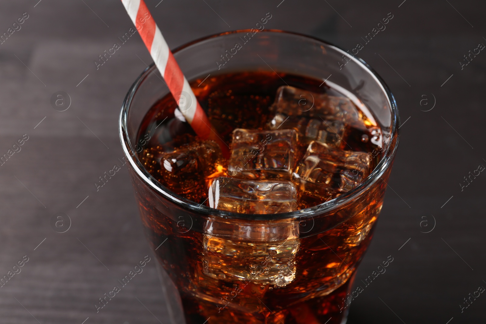 Photo of Refreshing cola with ice cubes and drinking straw in glass on black wooden table, closeup