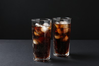 Photo of Refreshing cola with ice cubes in glasses on black table, closeup