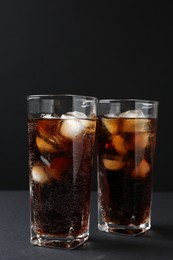 Photo of Refreshing cola with ice cubes in glasses on black table, closeup