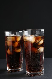 Photo of Refreshing cola with ice cubes in glasses on black table, closeup