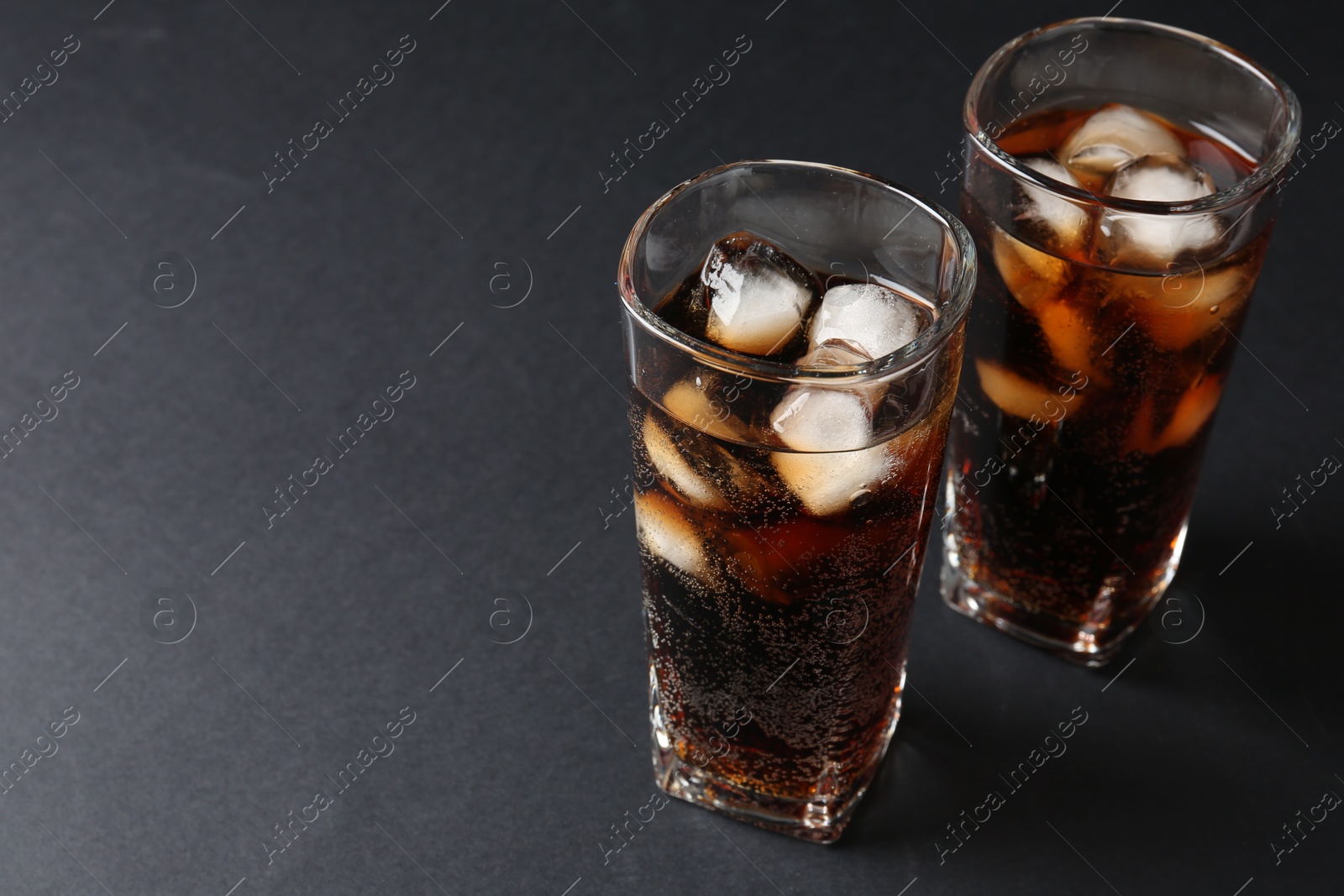 Photo of Refreshing cola with ice cubes in glasses on black table, closeup. Space for text