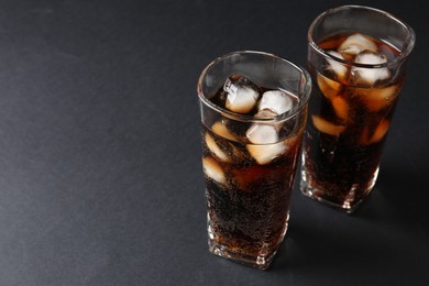 Photo of Refreshing cola with ice cubes in glasses on black table, closeup. Space for text