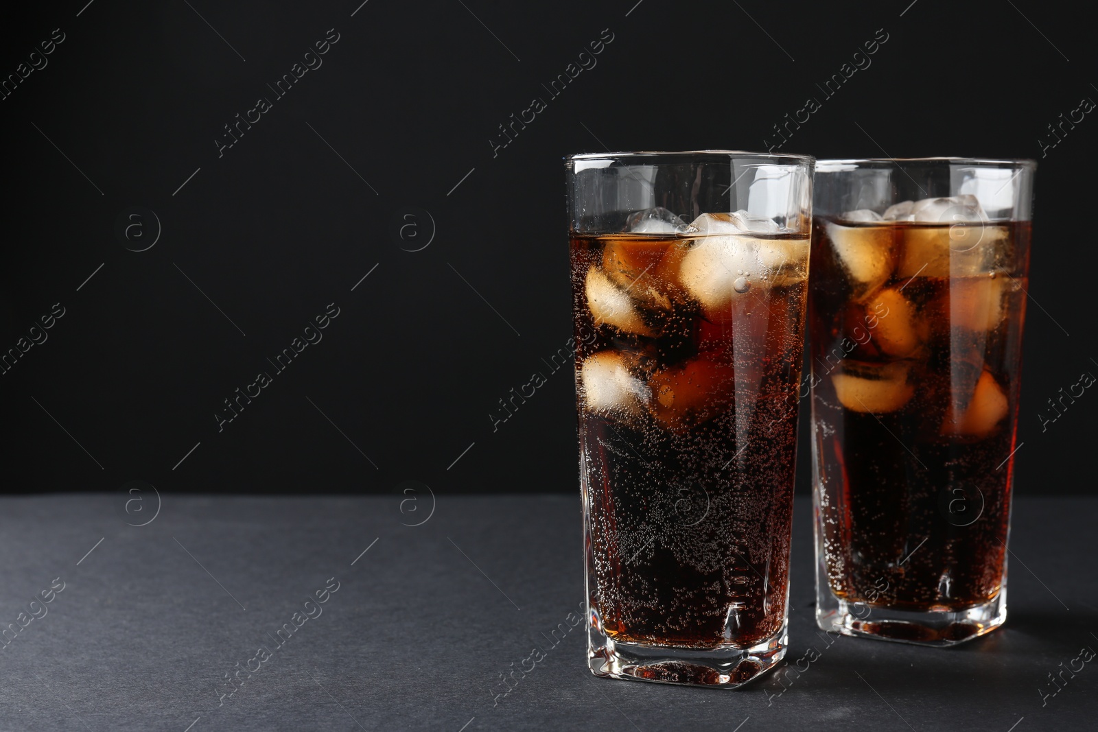 Photo of Refreshing cola with ice cubes in glasses on black table, closeup. Space for text