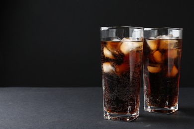 Photo of Refreshing cola with ice cubes in glasses on black table, closeup. Space for text