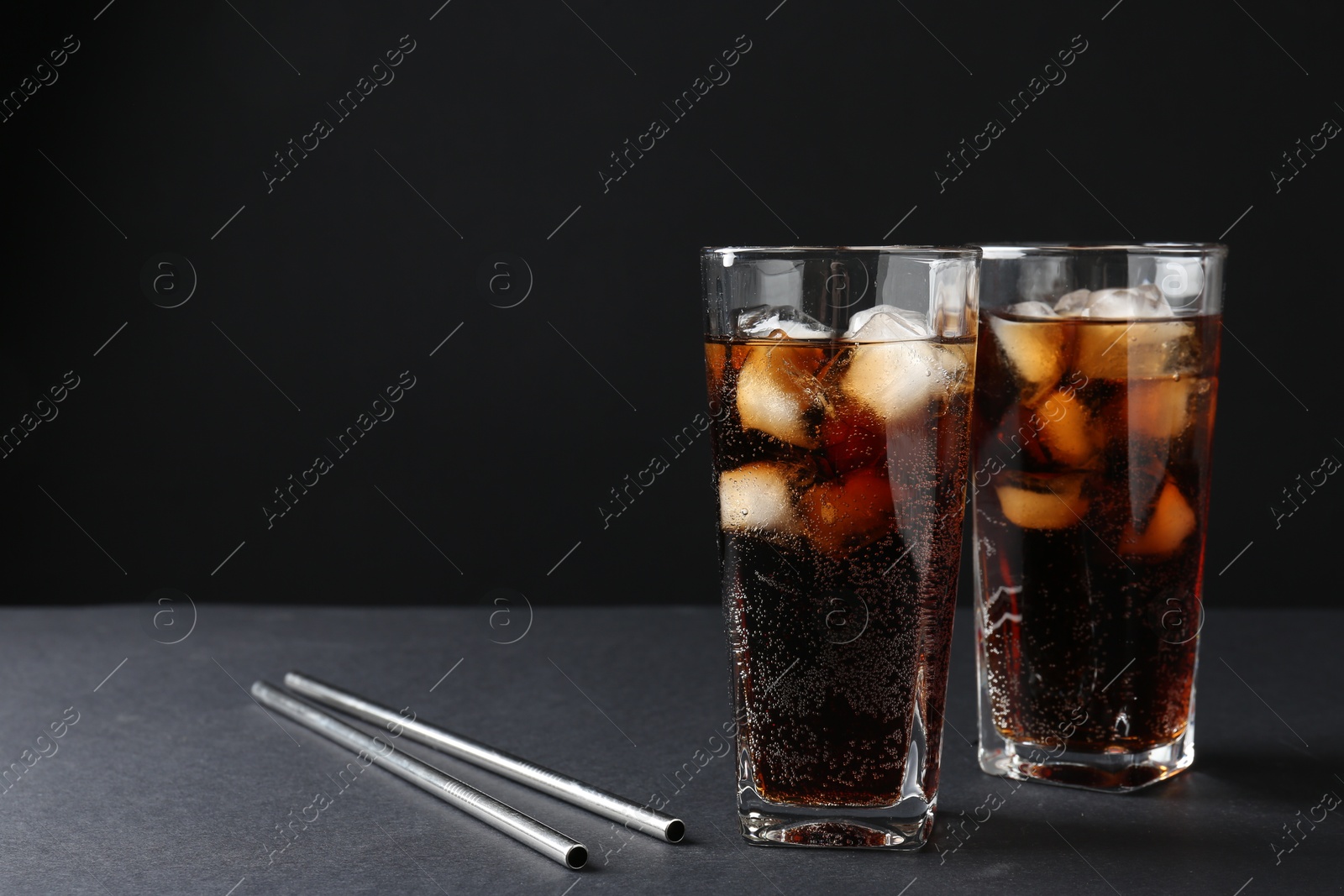 Photo of Refreshing cola with ice cubes in glasses and drinking straws on black table, closeup. Space for text