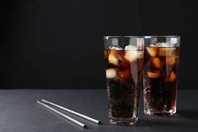 Refreshing cola with ice cubes in glasses and drinking straws on black table, closeup. Space for text