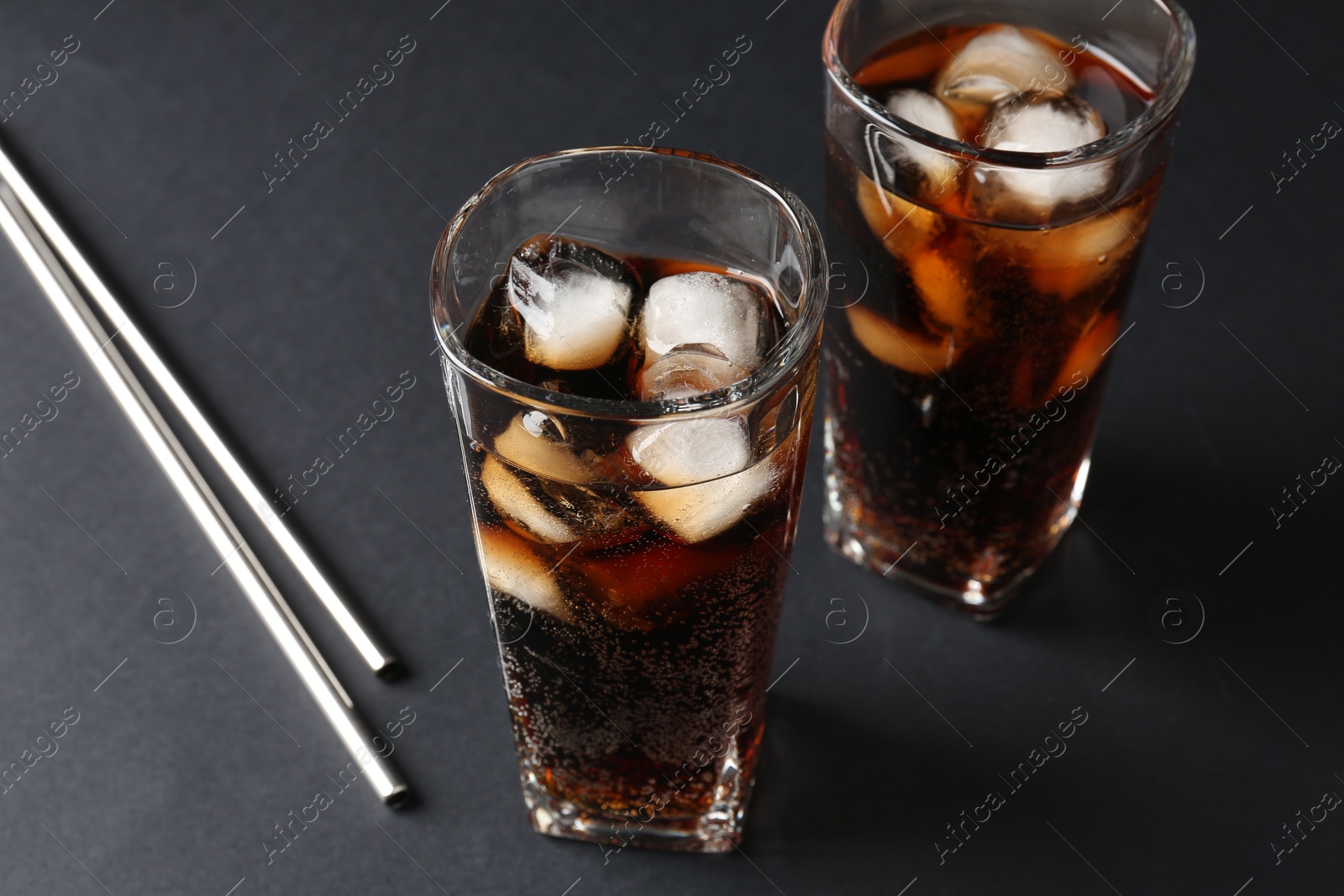 Photo of Refreshing cola with ice cubes in glasses and drinking straws on black table, closeup