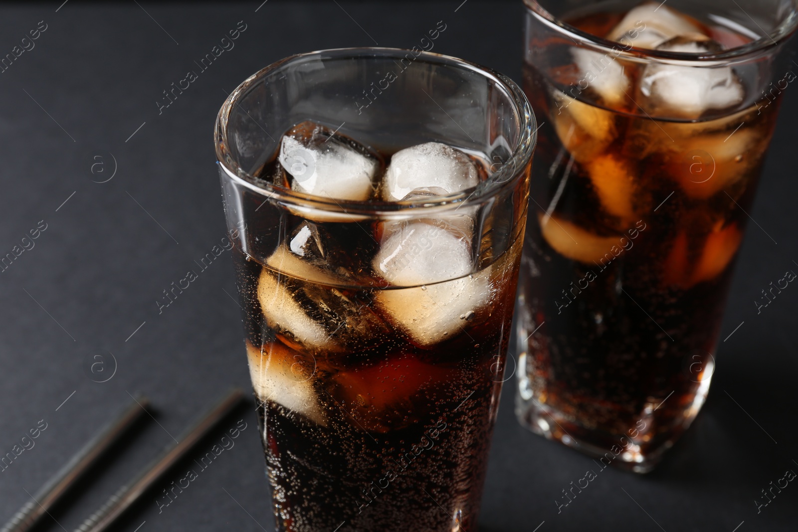 Photo of Refreshing cola with ice cubes in glasses and drinking straws on black table, closeup