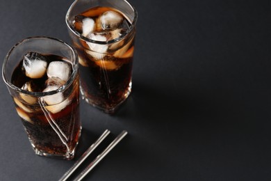 Photo of Refreshing cola with ice cubes in glasses and drinking straws on black table, closeup. Space for text