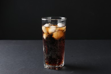 Photo of Refreshing cola with ice cubes in glass on black table, closeup