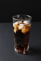 Photo of Refreshing cola with ice cubes in glass on black table, closeup