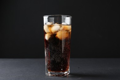 Photo of Refreshing cola with ice cubes in glass on black table, closeup