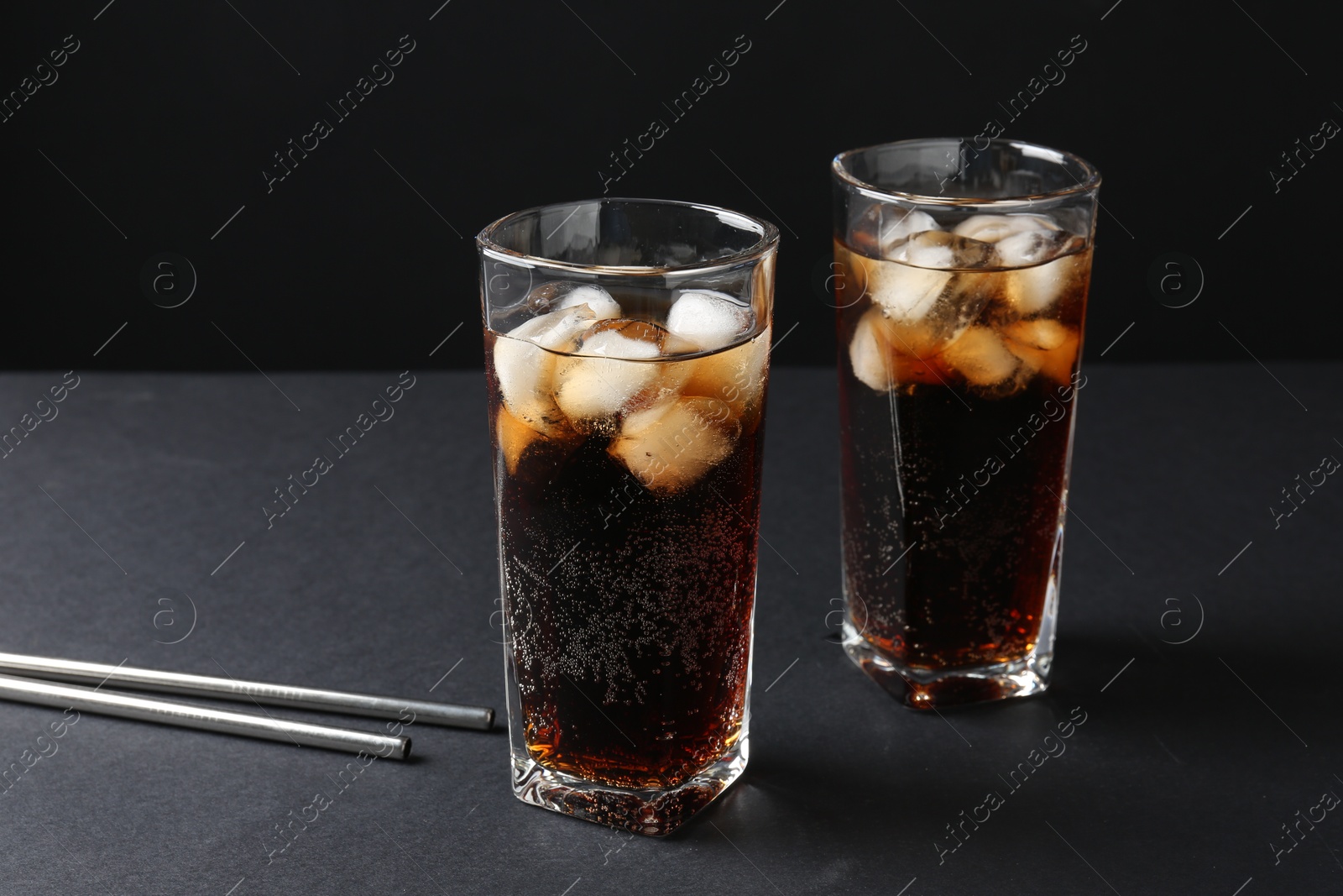 Photo of Refreshing cola with ice cubes in glasses and drinking straws on black table, closeup