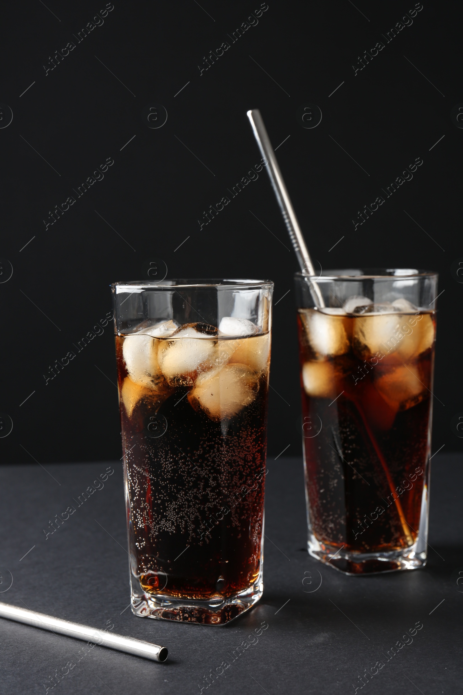 Photo of Refreshing cola with ice cubes in glasses and drinking straws on black table, closeup