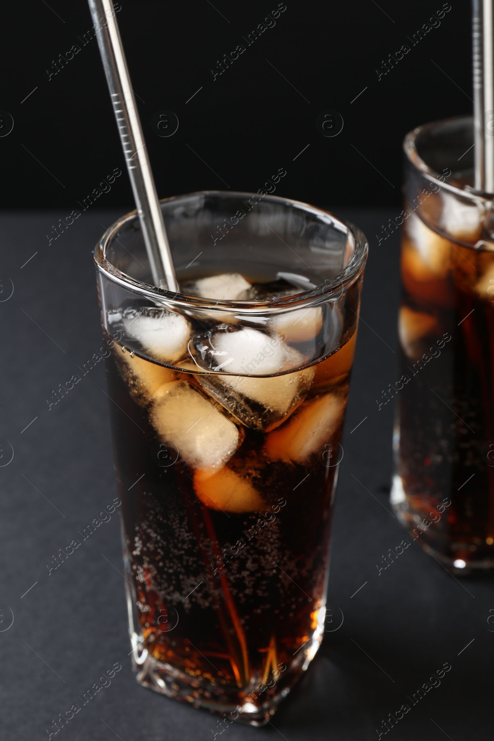 Photo of Refreshing cola with ice cubes and drinking straws in glasses on black table, closeup