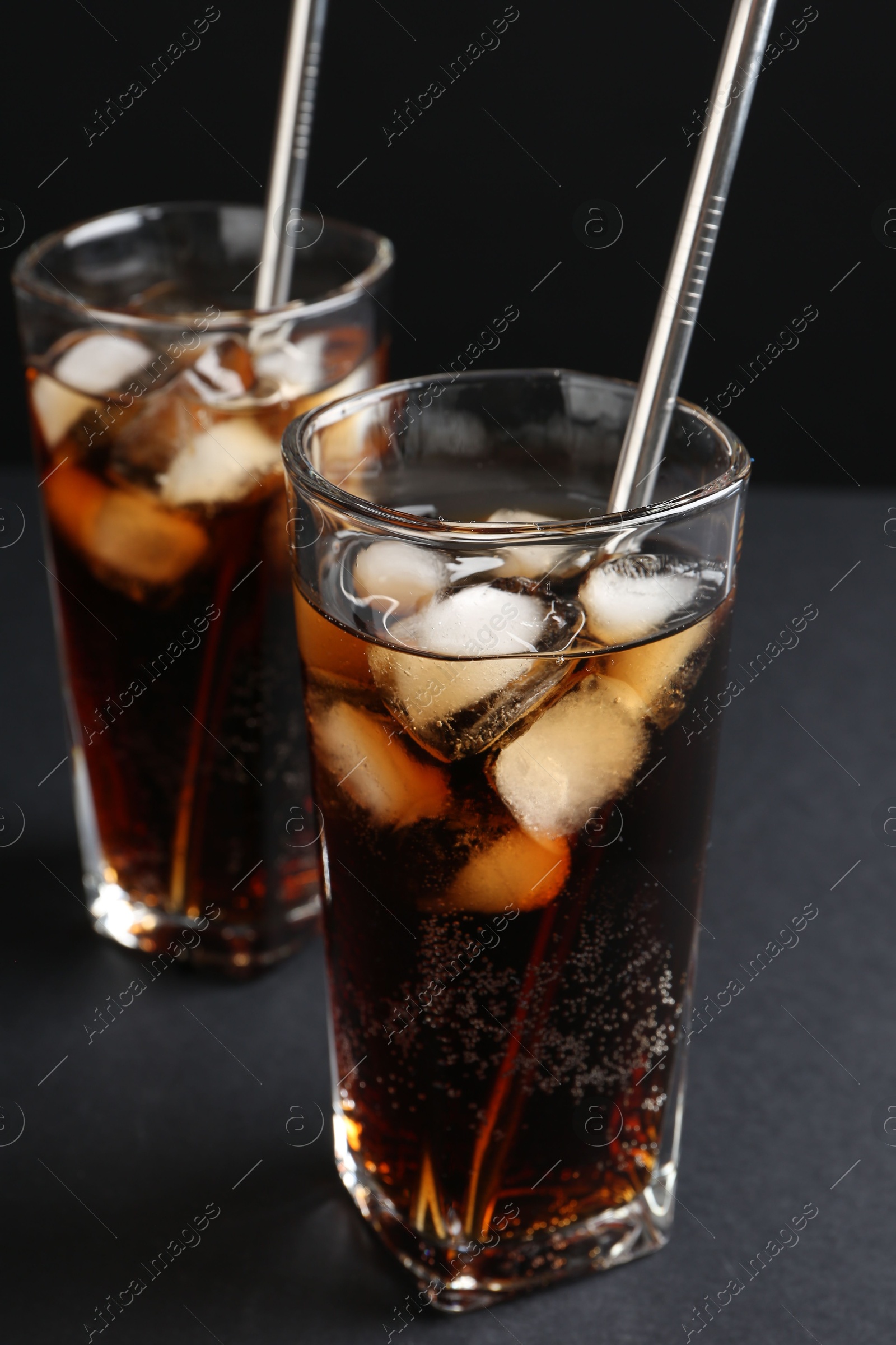 Photo of Refreshing cola with ice cubes and drinking straws in glasses on black table, closeup