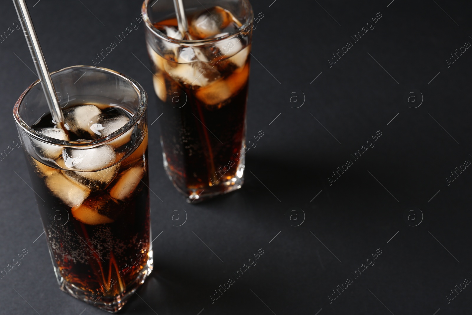 Photo of Refreshing cola with ice cubes and drinking straws in glasses on black table, closeup. Space for text