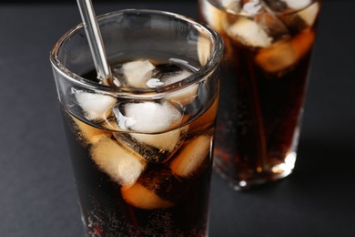 Refreshing cola with ice cubes in glasses on black table, closeup