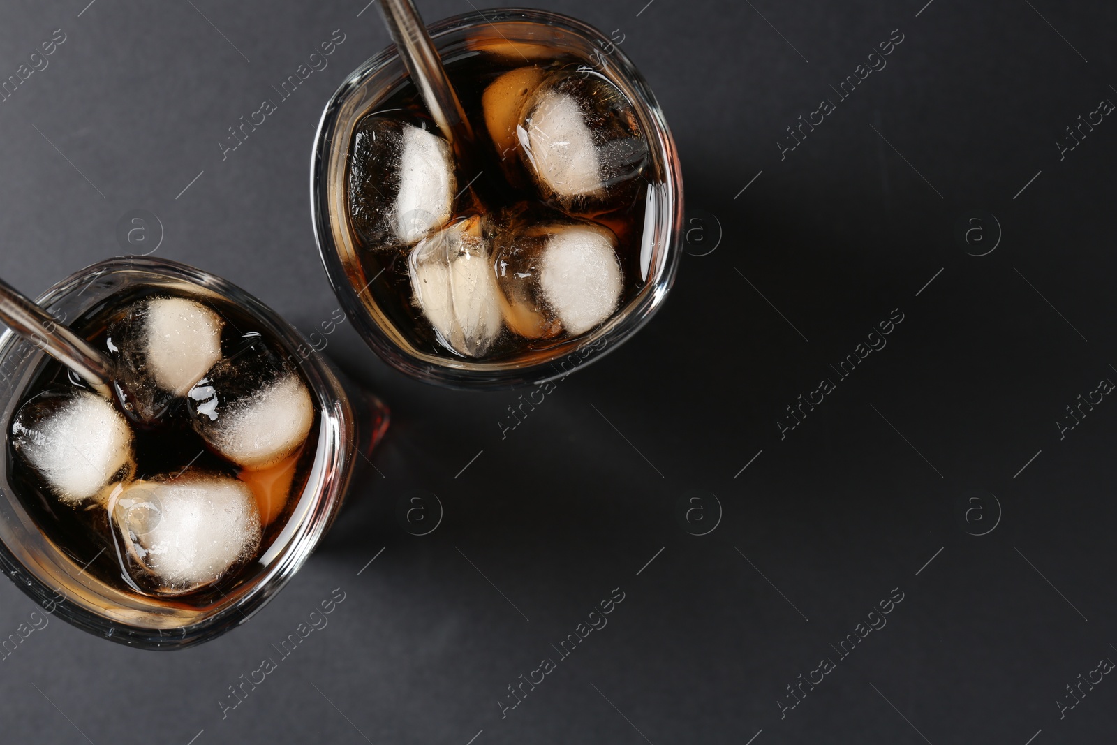 Photo of Refreshing cola with ice cubes and drinking straws in glasses on black table, flat lay. Space for text