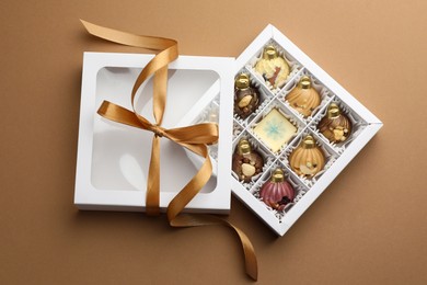 Photo of Open box with delicious chocolate in shape of Christmas ornaments on beige background, top view