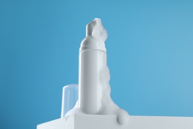 Photo of Bottle of cosmetic product with foam on podium against light blue background