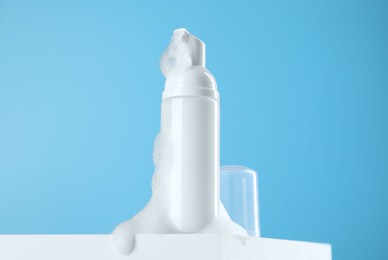 Bottle of cosmetic product with foam on podium against light blue background