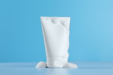 Photo of Tube of cosmetic product with foam on light blue background