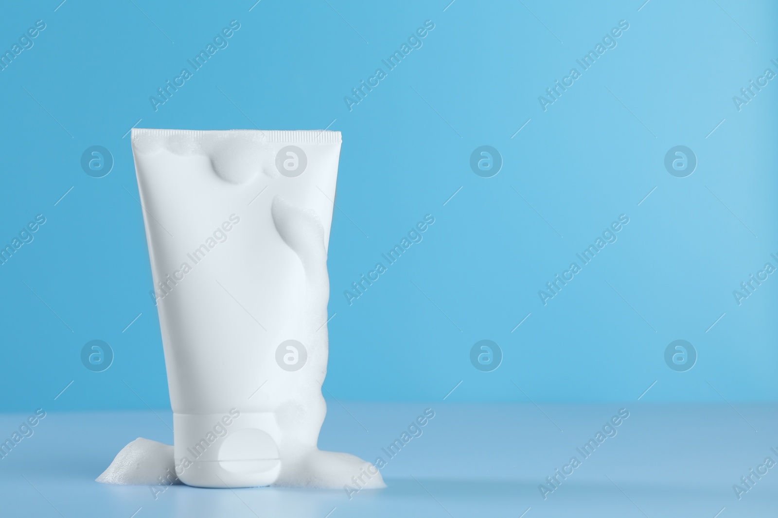 Photo of Tube of cosmetic product with foam on light blue background, space for text