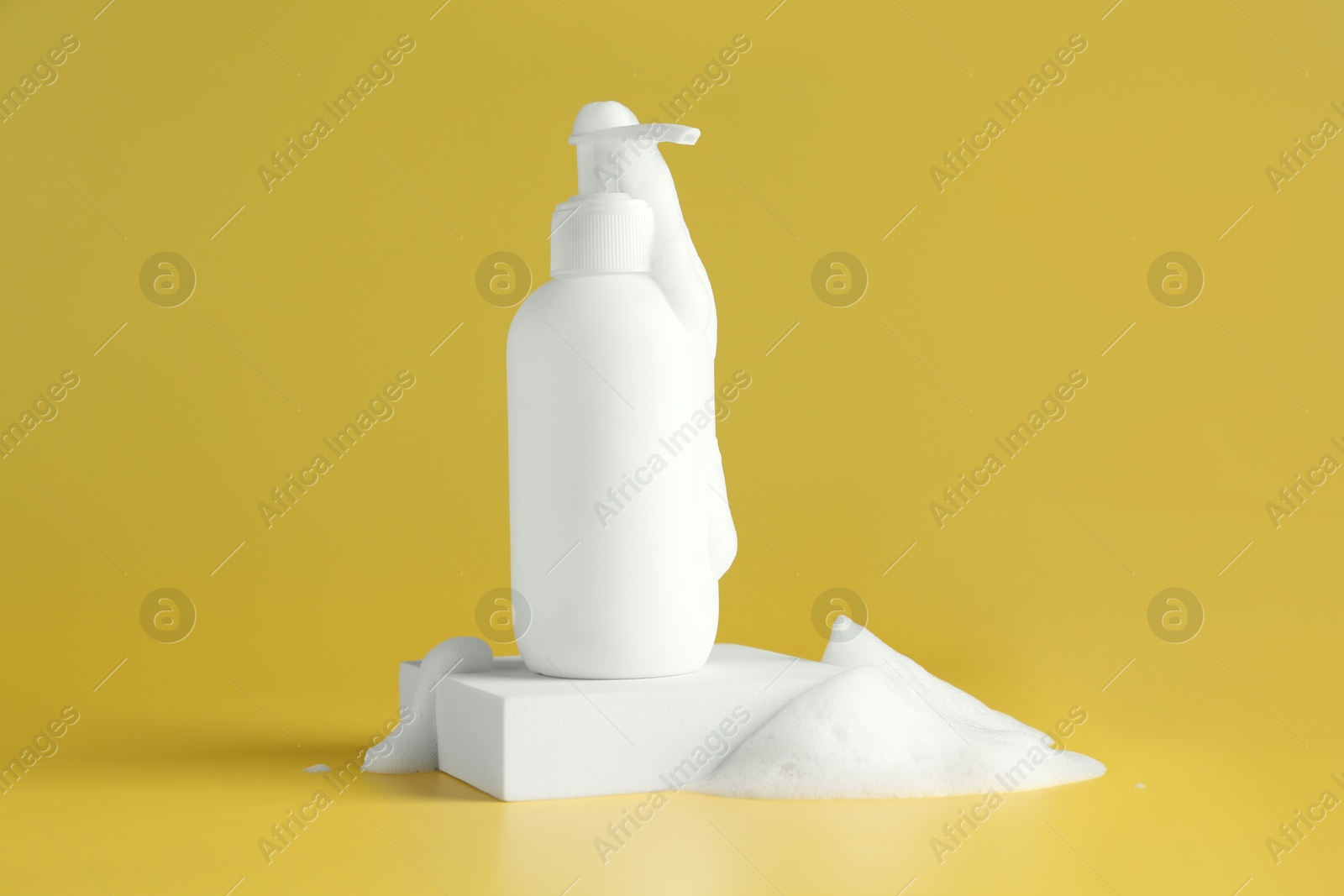 Photo of Bottle of cosmetic product with foam on podium against yellow background