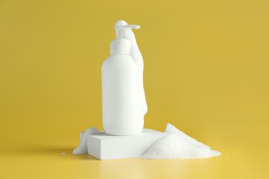 Photo of Bottle of cosmetic product with foam on podium against yellow background