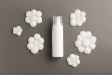 Bottle of cosmetic product with foam in shape of flowers on grey background, top view